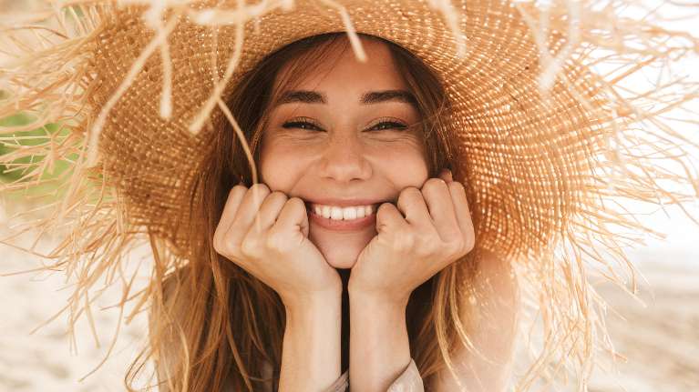 A smiling woman in a straw hat on the beach | dentist charlestown nsw
